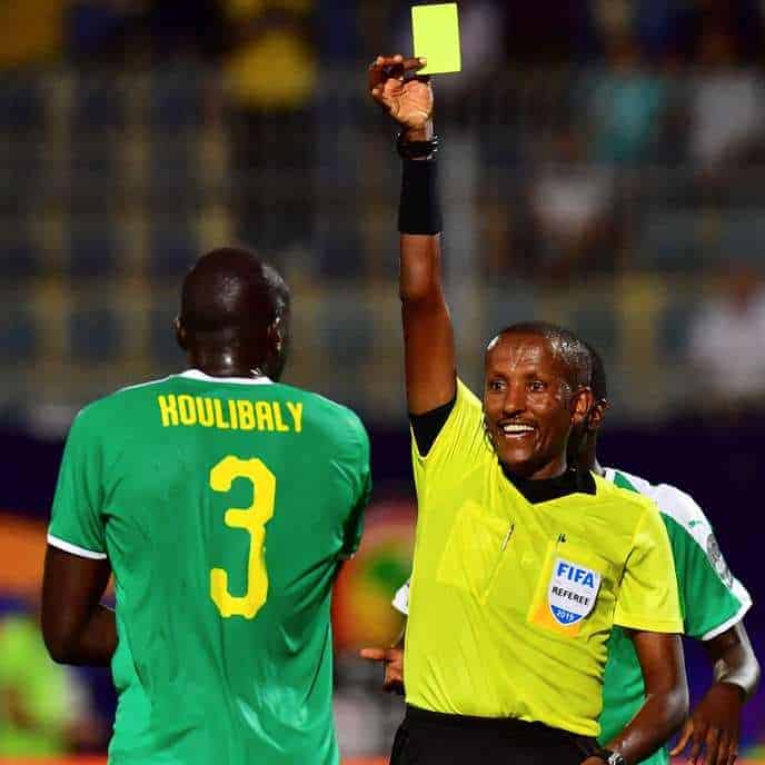 Ethiopian referee Bamlak Tessema Weyesa shows a yellow card to Senegal's defender Kalidou Koulibaly (L) during the 2019 Africa Cup of Nations (CAN) Semi-final football match between Senegal and Tunisia at the 30 June stadium in Cairo on July 14, 2019. (Photo by Giuseppe CACACE / AFP)