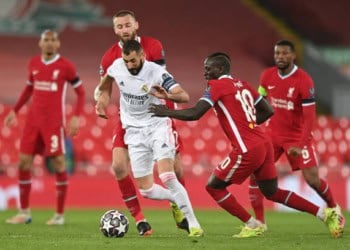 LIVERPOOL, ENGLAND - APRIL 14: Karim Benzema of Real Madrid is challenged by Nathaniel Phillips and Sadio Mane of Liverpool during the UEFA Champions League Quarter Final Second Leg match between Liverpool FC and Real Madrid at Anfield on April 14, 2021 in Liverpool, England. Sporting stadiums around the UK remain under strict restrictions due to the Coronavirus Pandemic as Government social distancing laws prohibit fans inside venues resulting in games being played behind closed doors. (Photo by Shaun Botterill/Getty Images)